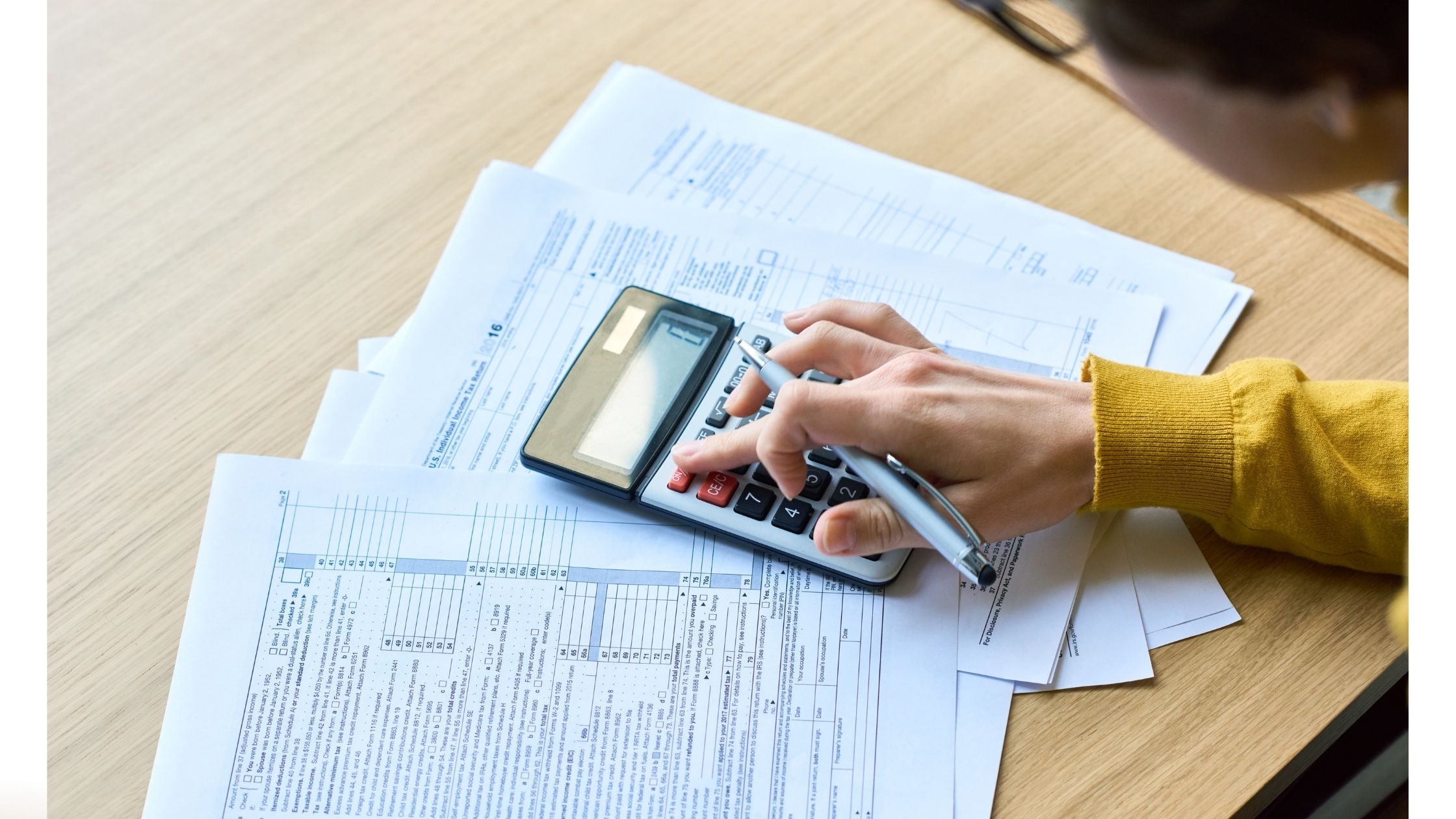 Photo of a hand on a desk, filling out tax forms using a calculator