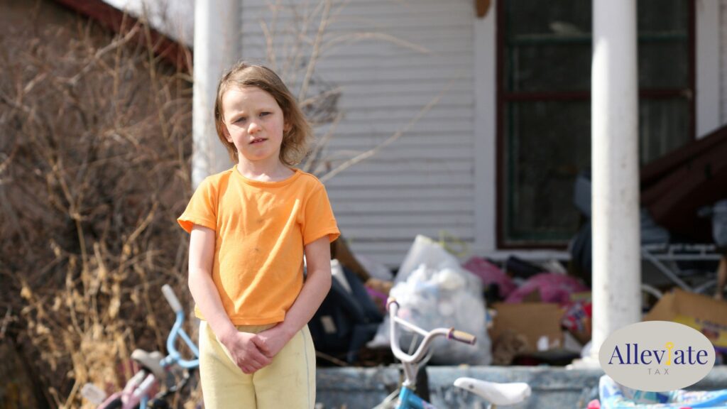 Child stands in front of a cluttered house