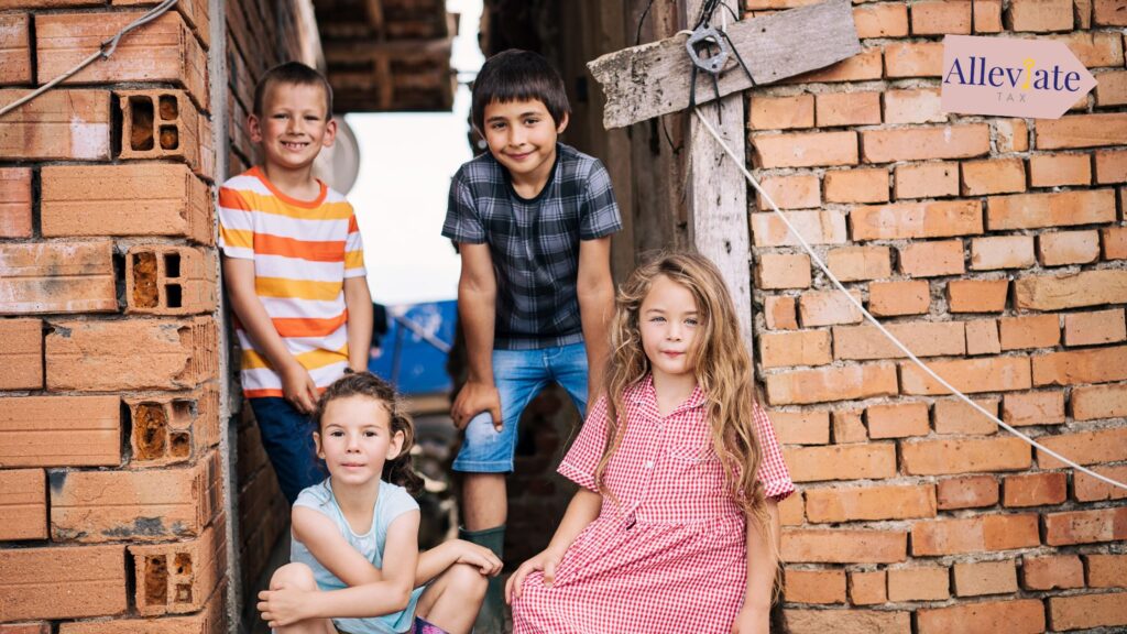 Four children sit in front of a run-down brick building