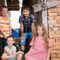 Four children sit in front of a run-down brick building